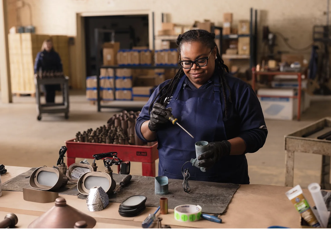 A CopperMoon team member assembling copper fixtures at a workbench in the West Point warehouse